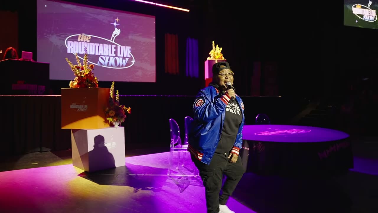 Host on stage with the Roundtable Live Show projection graphics behind him