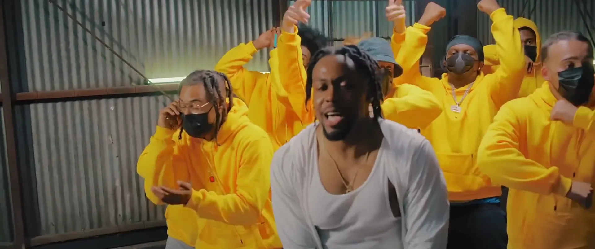 The artist performing in a white shirt in front of a crowd in yellow hoodies, from the No Call Back video