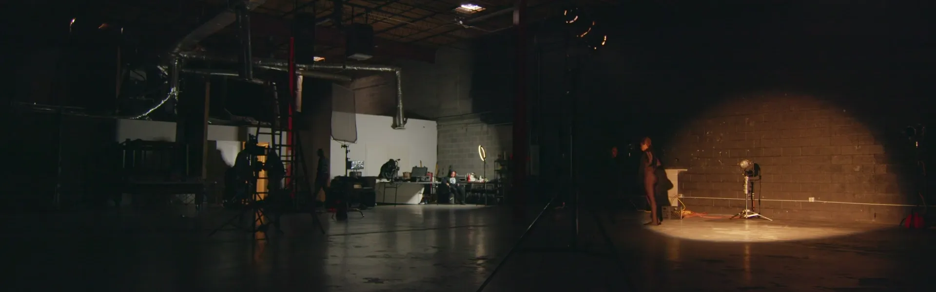 A High Arc crew lighting a warehouse set, one hard light pooled on the back wall