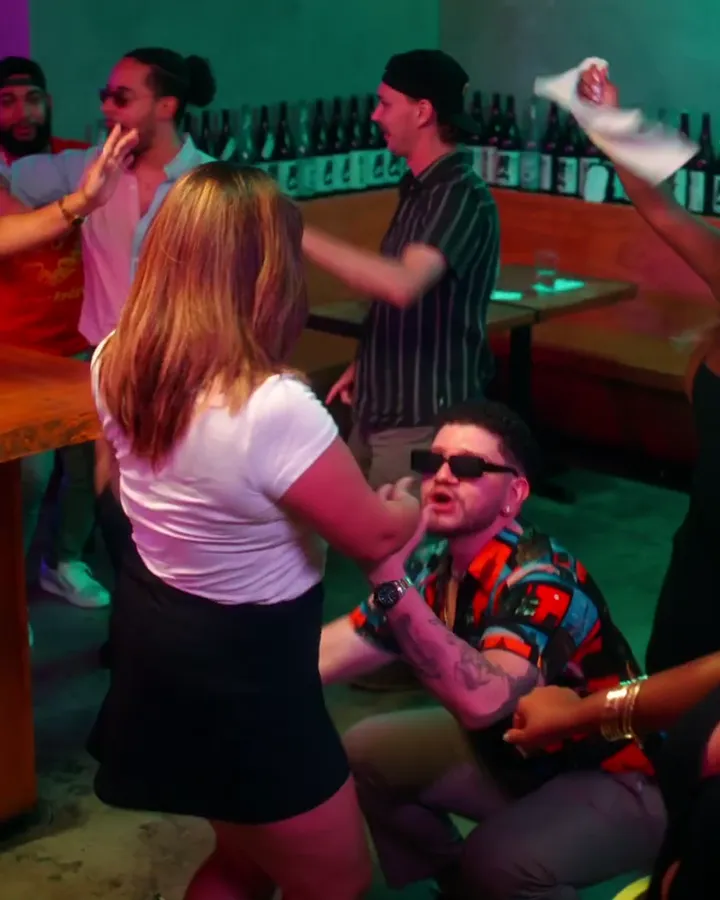 A neon-lit bar set with cast dancing, from Toxicat
